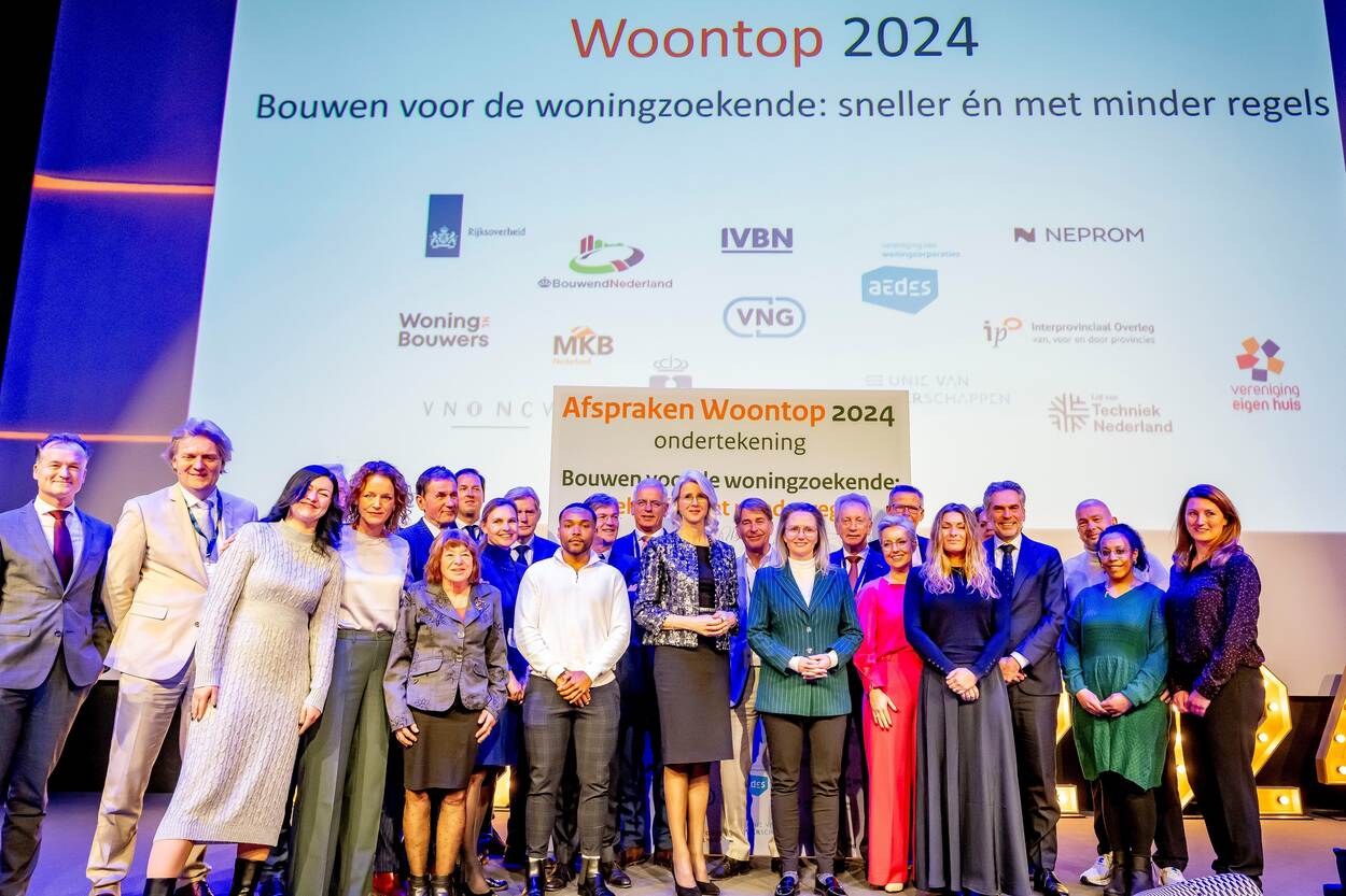 Groepsfoto met deelnemers van de Woontop 2024 voor het bord met de ondertekeningen