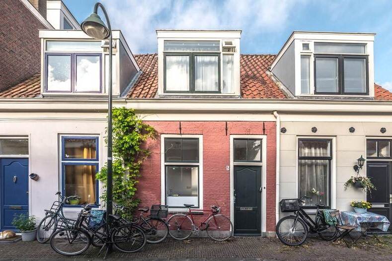 Foto van een rijtje met drie kleine, oude huizen. Het middelste huis is roze geverfd